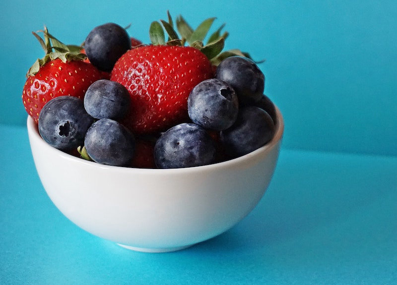 A bowl of berries like strawberries and blueberries against a blue background